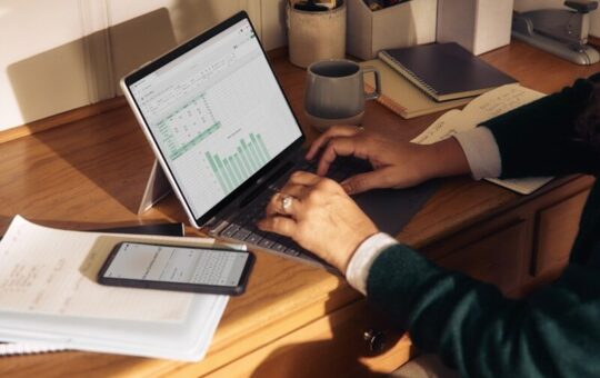 Person working on laptop at a wooden desk.